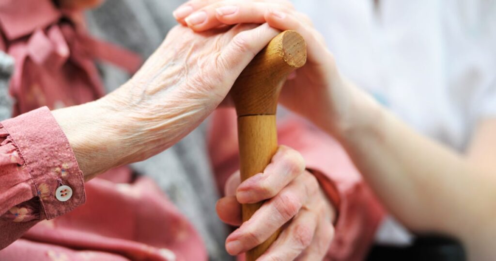 elder lady is holding a walking stick.