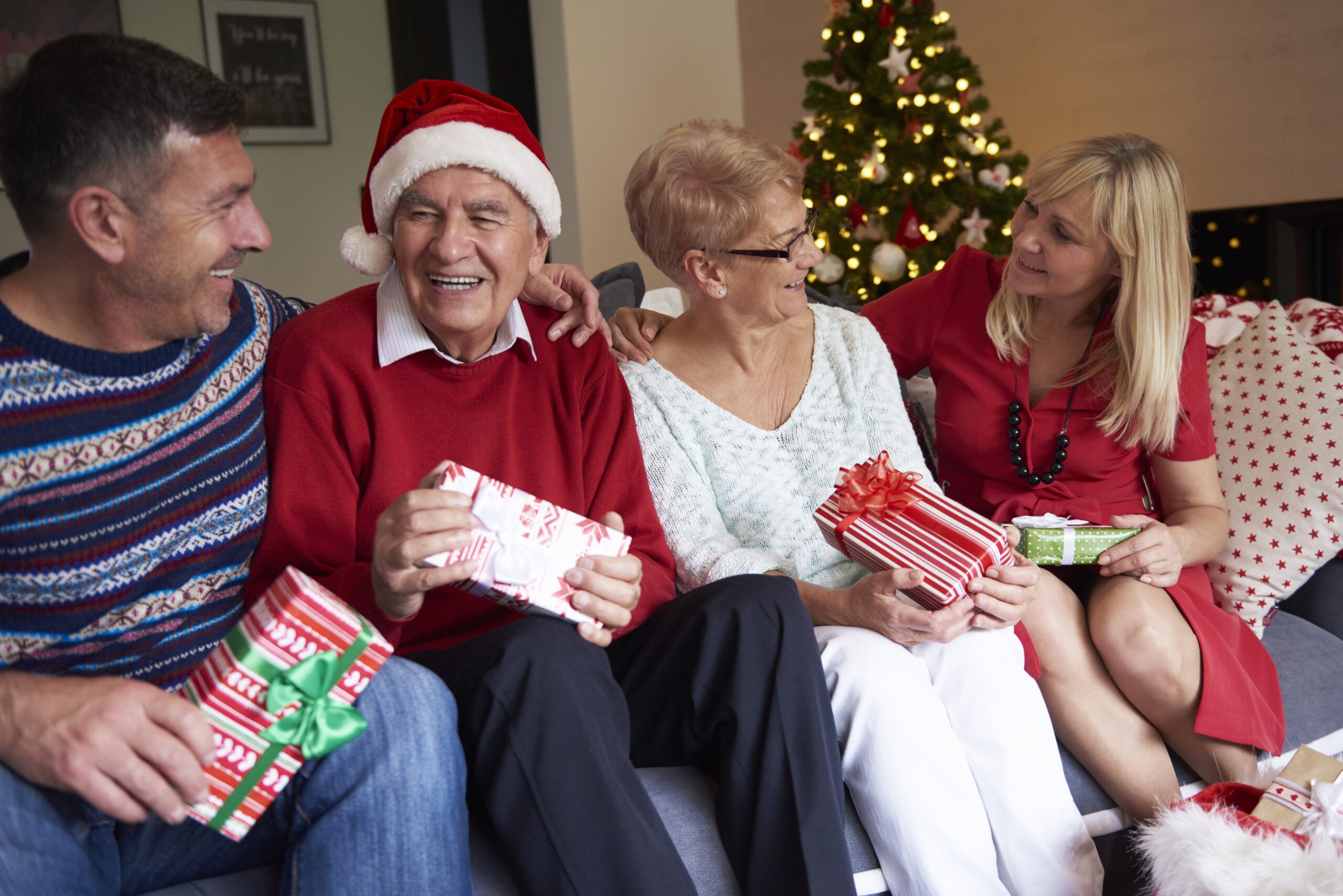 Four people in the living room on Christmas Adult children visiting ageing parents at Christmas, sitting together and exchanging gifts