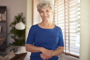 Older woman standing near a window at home, illustrating aged care reforms & the No Worse Off principle.
