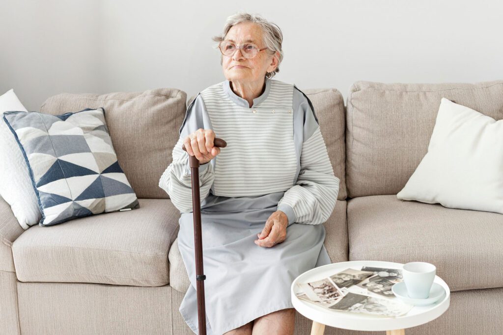 Elderly woman with walking stick sitting on sofa