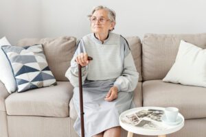 Elderly woman with walking stick sitting on sofa
