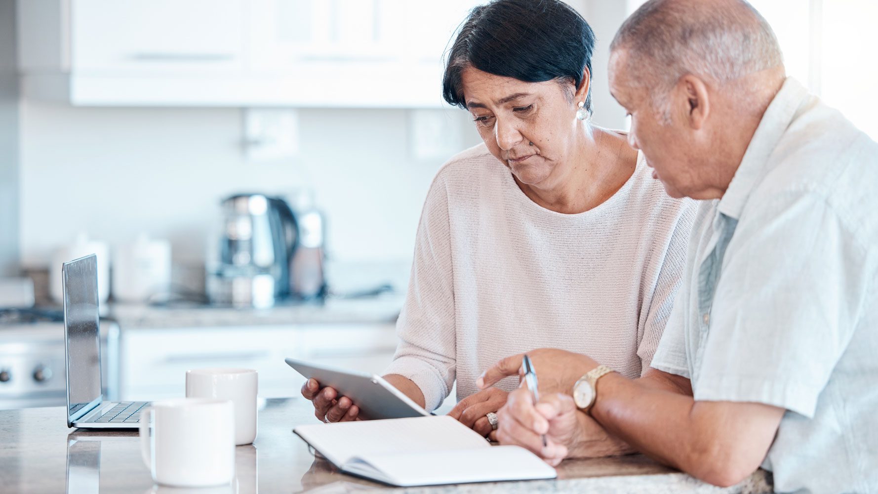 Senior couple at kitchen bench with laptop budgeting