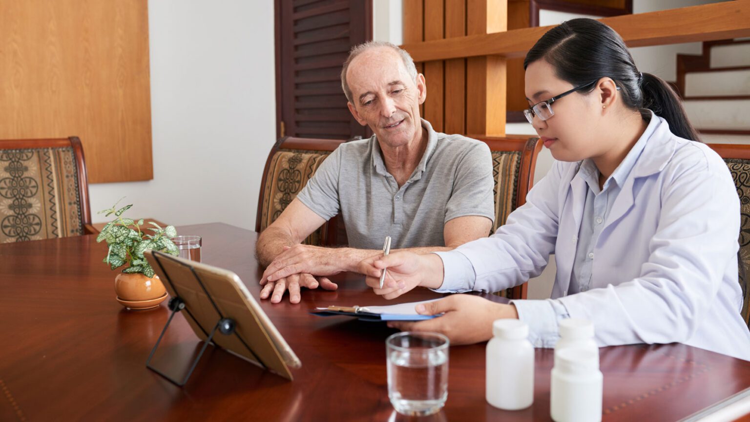 Elderly man with with care manager sitting at table with tablet.