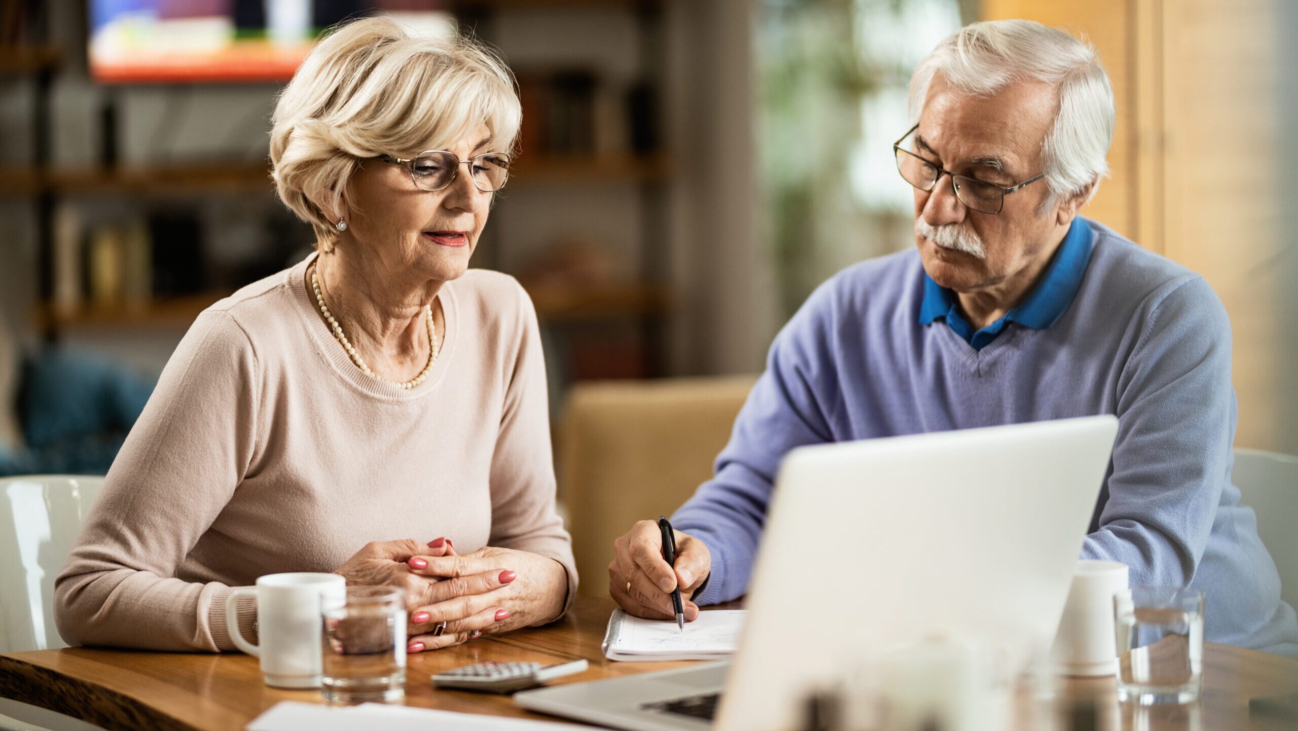 Mature couple using computer while planning their home budget. Mature couple at table with laptop discussing aged care fees