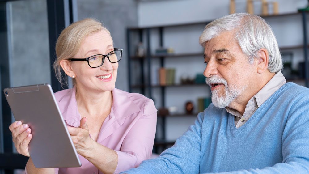 An older man and woman sitting at a table with a tablet