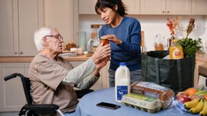 Elderly man in wheelchair unpacking shopping with home support worker