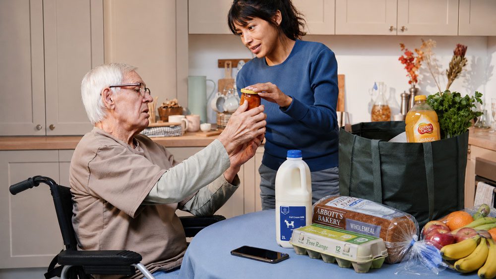 Elderly man in wheelchair unpacking shopping with home support worker