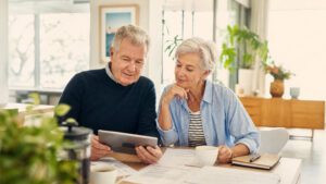 Senior couple at table with paper work and tablet checking assets and income
