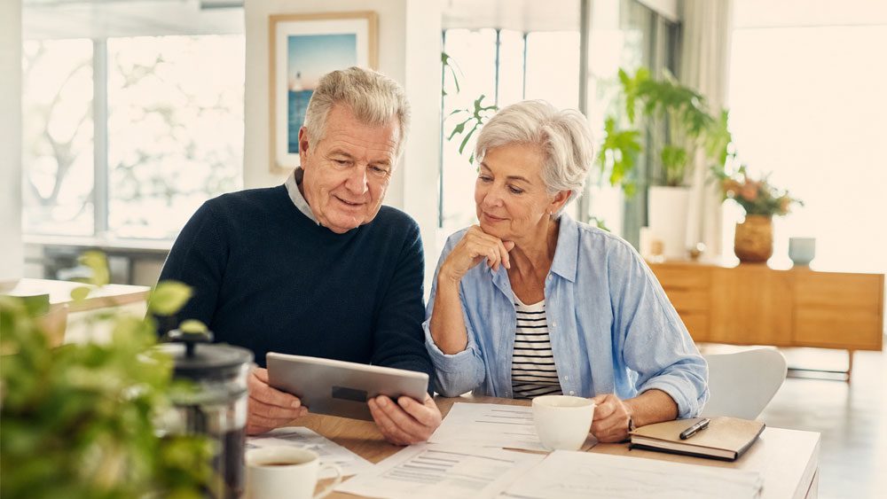 Senior couple at table with paper work and tablet checking assets and income